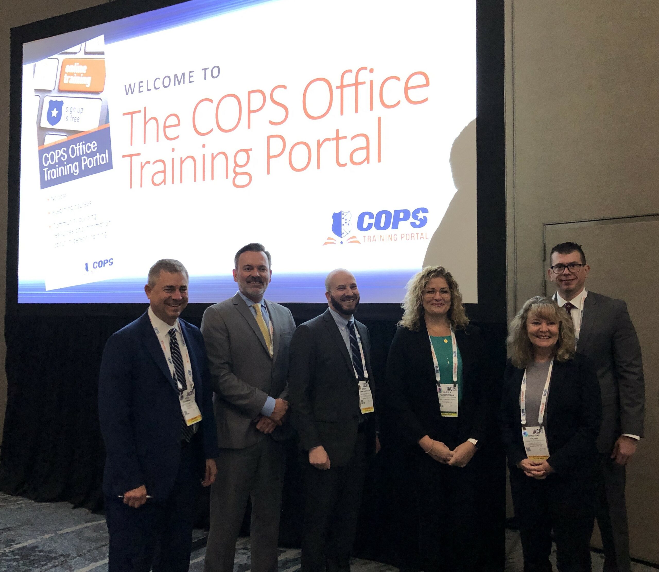 Five professionals posed in front of a screen prepared for a presentation on the COPS Training Portal.